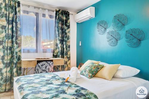 1 dormitorio con cama y pared azul en Villa Flamants - Terrasse & Jacuzzi - Saint-Joseph, en Saint-Joseph