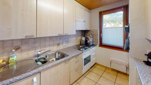 cocina con armarios blancos, fregadero y ventana en Chalet Leonie LE0, en Blatten bei Naters