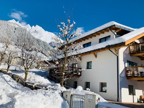 ein schneebedecktes Gebäude mit einem Baum und Bergen in der Unterkunft Bacher Ferienwohnungen in Virgen
