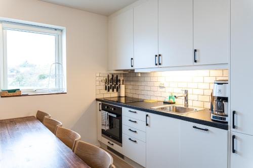 cocina con armarios blancos y mesa de madera en New Åkrahamn coast house, en Sæveland