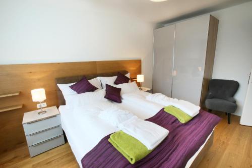 a large bed with white sheets and purple and green pillows at Seehaus LakeSide - Am Hafen in Neusiedl am See