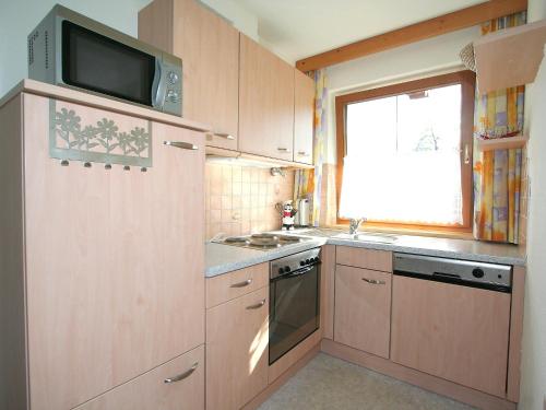eine Küche mit Holzschränken, einer Mikrowelle und einem Fenster in der Unterkunft Apartment Herbert-1 by Interhome in Emberg