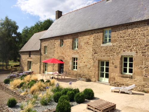 a large brick building with a table and a red umbrella at Holiday Home La Tronçonnais by Interhome in Les Portes du Coglais