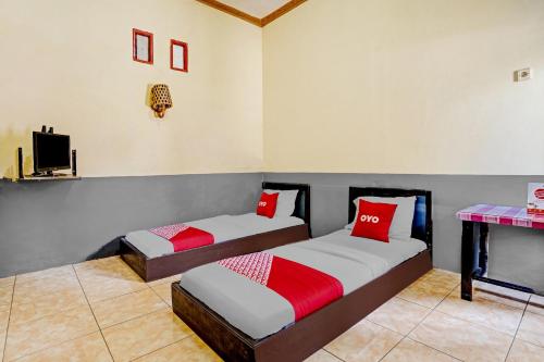 two beds with red pillows in a room at SUPER OYO 90405 Penginapan Sasti Kuningan in Cirebon