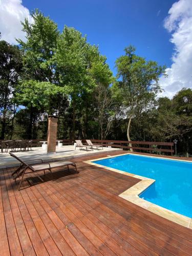 a swimming pool on a wooden deck with benches and trees at Pousada O Cantinho da Raposa in Monte Verde