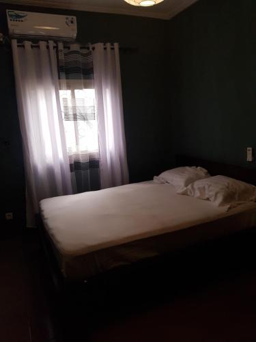 Una cama en un dormitorio con una ventana con sábanas blancas. en Superbe appartement en Duala