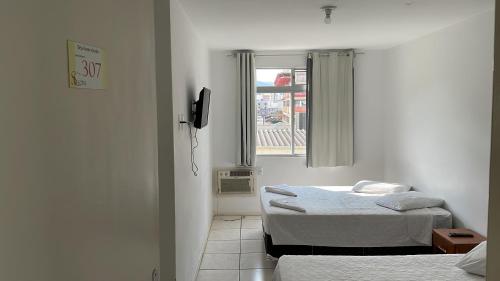 two beds in a small room with a window at Hotel San Carlos in Balneário Camboriú