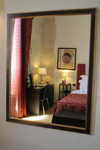 a mirror reflecting a bedroom with a bed and a desk at Domus Mariae Benessere in Siracusa