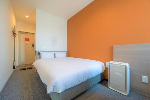 a large white bed in a room with an orange wall at HOTEL R9 The Yard Uruma in Uruma