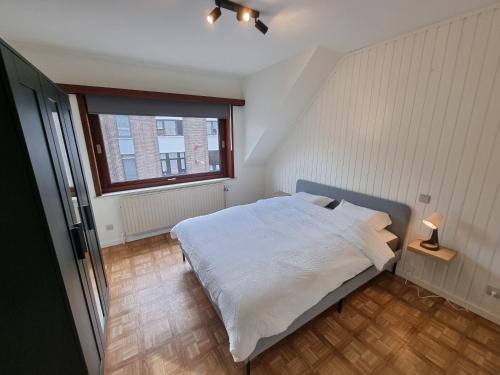 1 dormitorio con cama blanca y ventana en Duplex Appartement Opex, en Ostende