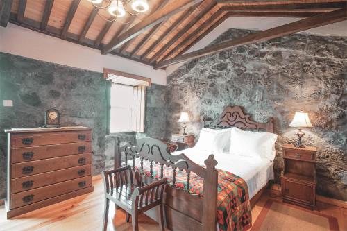 a bedroom with a bed and a dresser and a wall at Adegas do Pico in São Roque do Pico