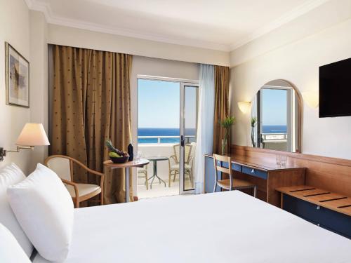 a hotel room with a bed and a desk and a room with the ocean at Esperides Beach Resort in Faliraki