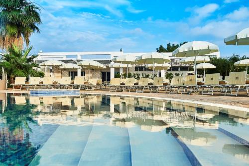 a swimming pool with chairs and umbrellas at Riva Marina Resort - CDSHotels in Carovigno