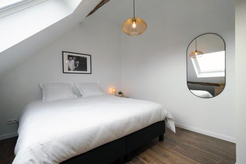 a white bedroom with a bed and a mirror at Gîtes des Remparts in Philippeville