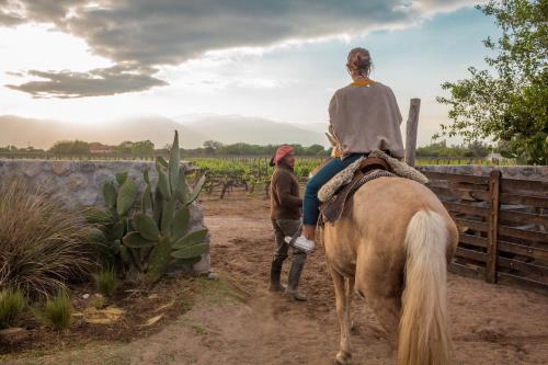 uma mulher montada num cavalo com um homem a andar atrás em Patios De Cafayate em Cafayate