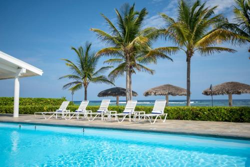 a pool with chairs and palm trees and the ocean at Le Soleil D'or in Cayman Brac