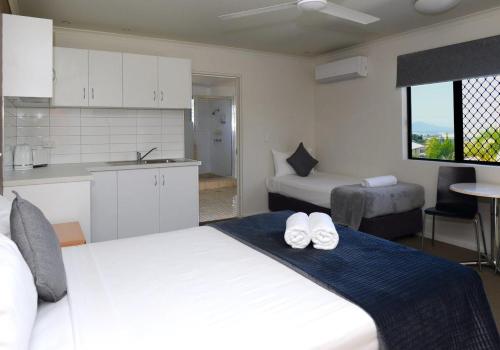 a bedroom with a large white bed and a kitchen at Summit Motel in Townsville