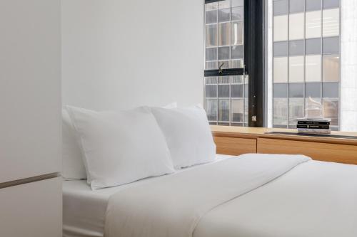 a white bed with white pillows and a window at Placemakr Wall Street in New York
