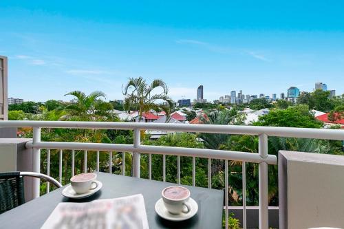 a table with two cups on a balcony with a view at The Wellington Apartment Hotel in Brisbane