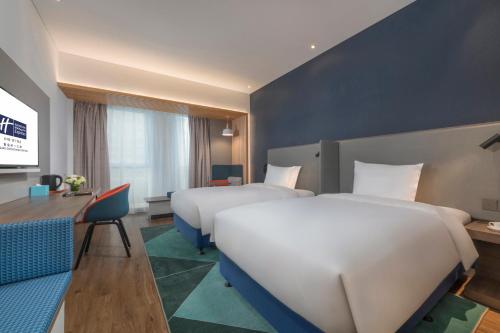 a hotel room with two beds and a desk at Holiday Inn Express Qingdao Chengyang Central by IHG in Qingdao