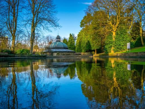 a pond in a park with a building and trees at Acorn Lodge Harrogate in Harrogate