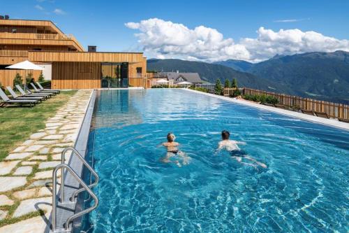two people are swimming in a swimming pool at Tratterhof Mountain Sky Hotel in Maranza