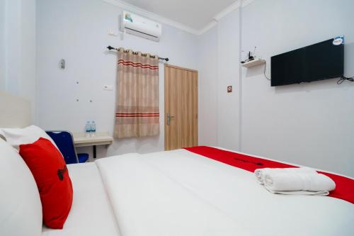 um quarto com uma cama branca com almofadas vermelhas e uma televisão em RedDoorz near Pantai Barat Pangandaran 2 em Pangandaran