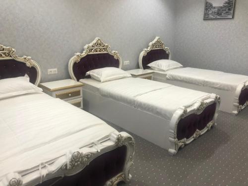 a room with three beds with white sheets at Suleyman hotel in Bukhara