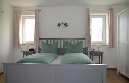 a bed with two green pillows and two windows at Ferienwohnung Anner Gstadt in Gstadt am Chiemsee