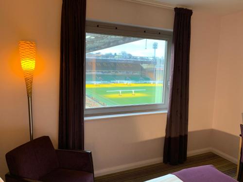 a bedroom with a window with a view of a baseball game at Holiday Inn Norwich City, an IHG Hotel in Norwich