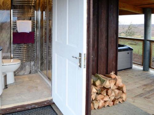 a bathroom with a door open with a pile of wood at Capercaillie Cottage in Rhilochan