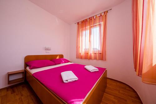 a bedroom with a pink bed with two towels on it at Željko Apartmani in Lopar
