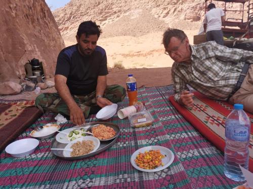 ワディ・ラムにあるGo bedouin campの二人の男がピクニック用の毛布に座って食べ物を持っている