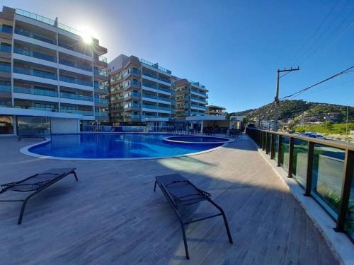 um deque com dois bancos e uma piscina em Apartamento Praia dos Anjos 2 Vagas de garagem e AR-CONDICIONADO em Arraial do Cabo