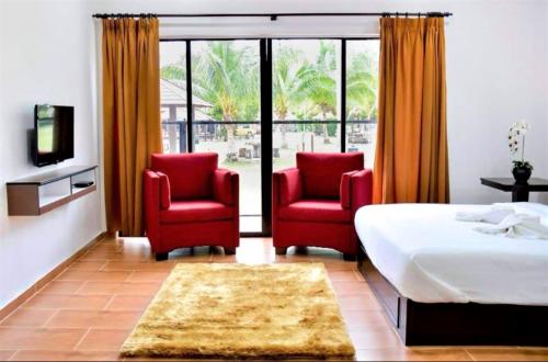 - une chambre avec deux chaises rouges et un lit dans l'établissement TELUK PENYABUNG RESORT, à Kampung Mawar