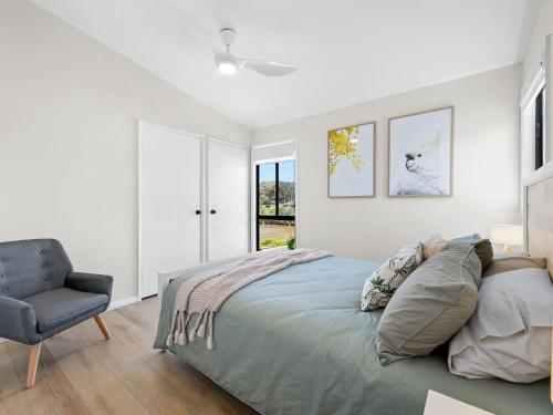 una camera da letto bianca con un letto e una sedia di Yabbarra Beach House a Dalmeny