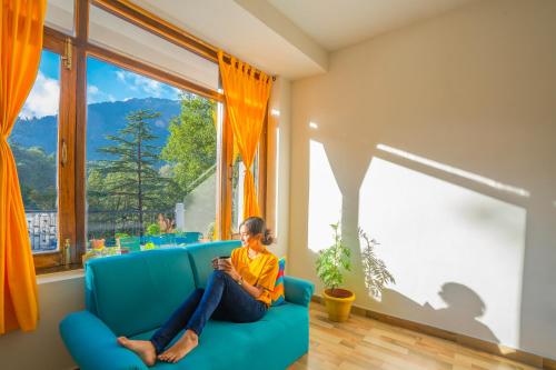 a woman sitting on a blue couch in a room with a window at goSTOPS Nainital in Nainital