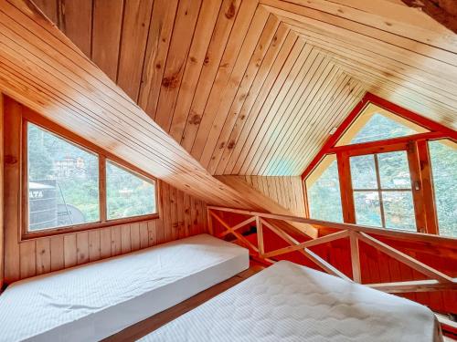 a room with two beds in a cabin with windows at Madpackers Jibhi - Of Streamsides & Waterfalls in Jibhi