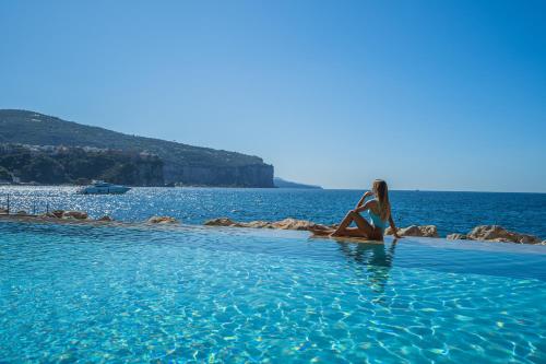 una donna seduta in una piscina vicino all'oceano di Capo la Gala Hotel&Wellness a Vico Equense