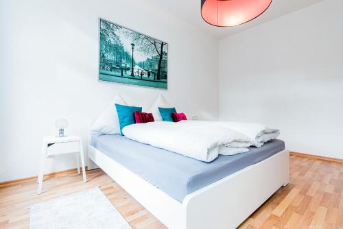 een witte slaapkamer met een bed met blauwe en rode kussens bij Helle Wohnung mit Balkon in grünen Innenhof - W-LAN, 4 Schlafplätze in Maagdenburg