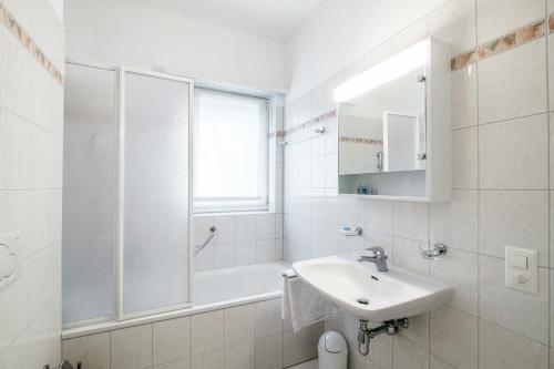 a white bathroom with a sink and a bath tub at Lido Apartments by Quokka 360 - 5 min from the centre and the Lugano Lido in Lugano