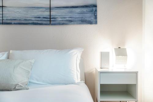 a bed with white pillows and a nightstand with a painting at Lido Apartments by Quokka 360 - 5 min from the centre and the Lugano Lido in Lugano