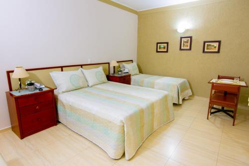 a hotel room with two beds and two tables at Hotel Iporã in Itapetininga
