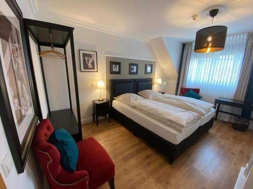 a bedroom with a large bed and a red chair at Hotel Hagspihl in Quakenbrück