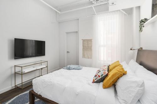 a white bedroom with a bed and a flat screen tv at Bakan - Sainte Catherine in Montréal