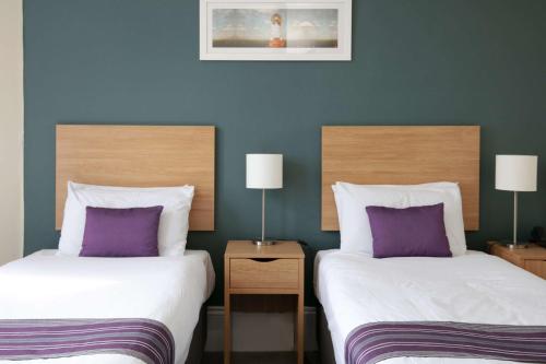 two beds in a hotel room with purple pillows at Exmouth Beach Hotel in Exmouth