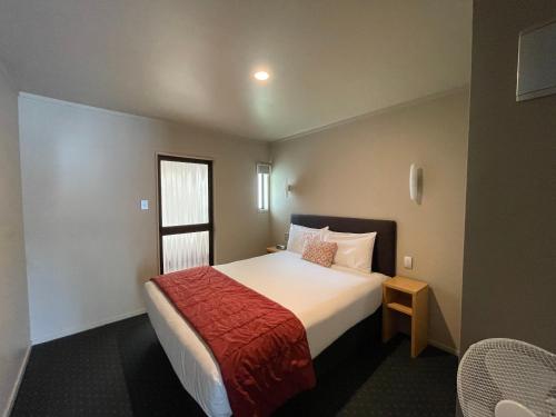 a bedroom with a large bed with a red blanket at Bentleys Motor Inn in Palmerston North