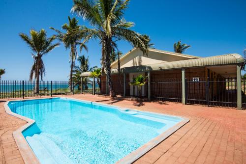 a swimming pool in front of a house with palm trees at Hedland Hotel in Port Hedland