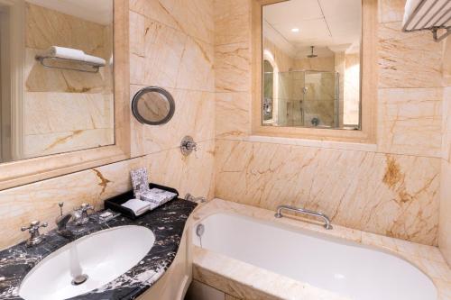 a bathroom with a tub and a sink and a mirror at The Claridges New Delhi in New Delhi