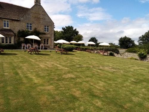 un grupo de mesas con sombrillas frente a un edificio en The Sibson Inn Hotel, en Water Newton